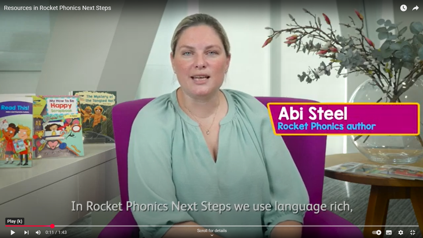 Author Abi Steel sits in a pink armchair next to Rocket Phoncs books as she talks through how to use the Next Steps programme